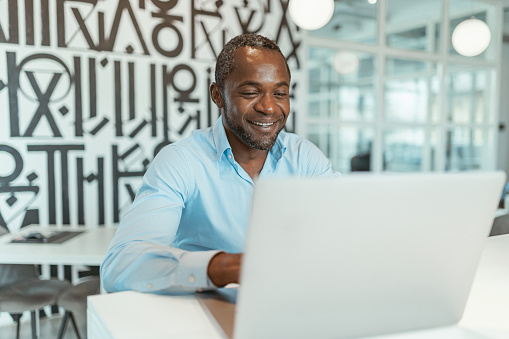 Smiling african businessman working laptop while sitting in modern coworking. High quality photo